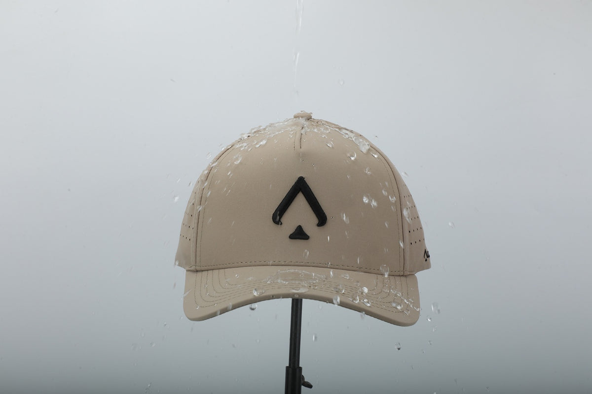 All In Lid Desert Sand hat, front view with water splashing off the crown and brim, showing the water resistant khaki fabric.