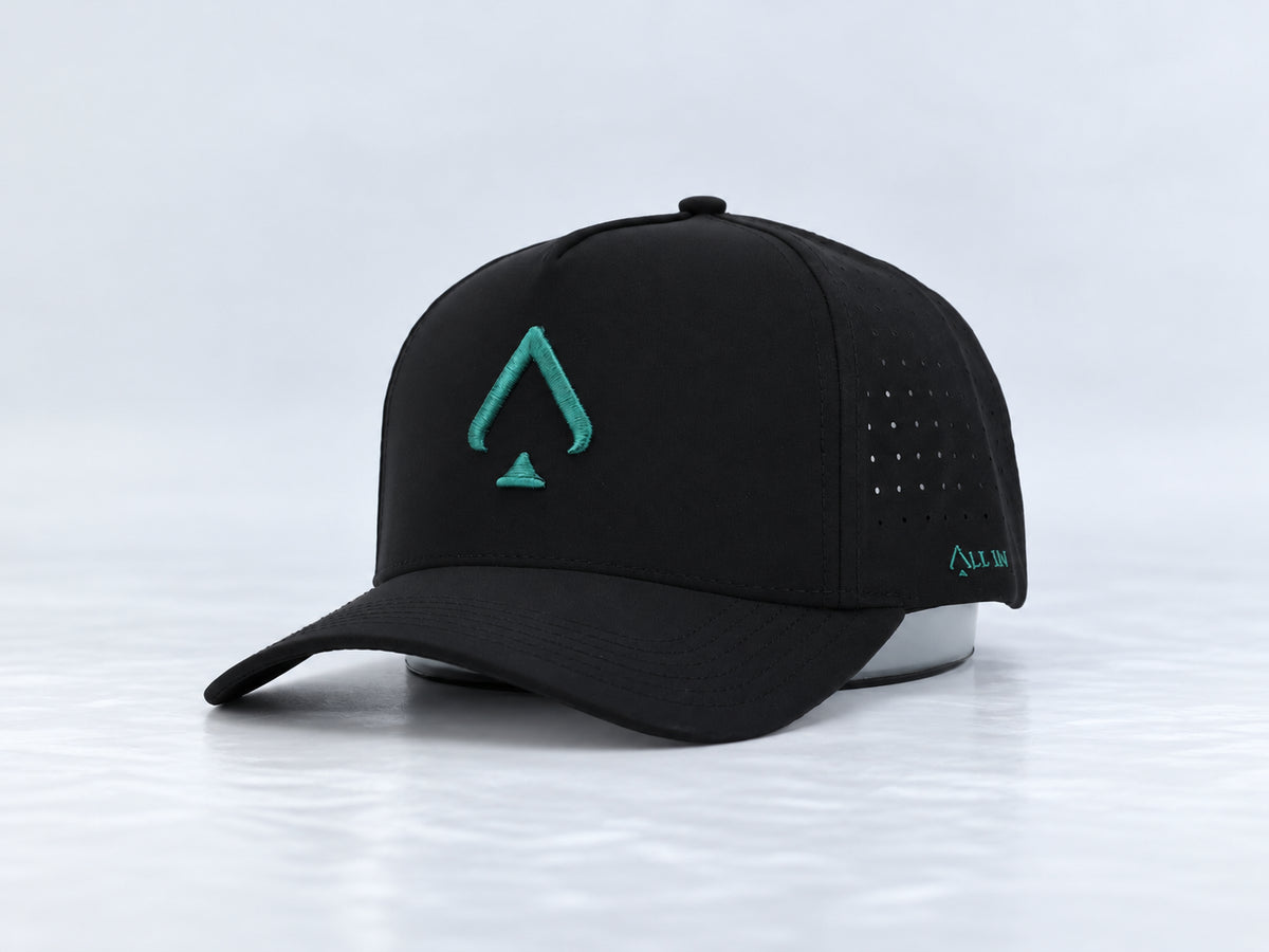 All In Lid Green Goblin black cap with teal green spade embroidery, front three-quarter view against a pale gray studio background.