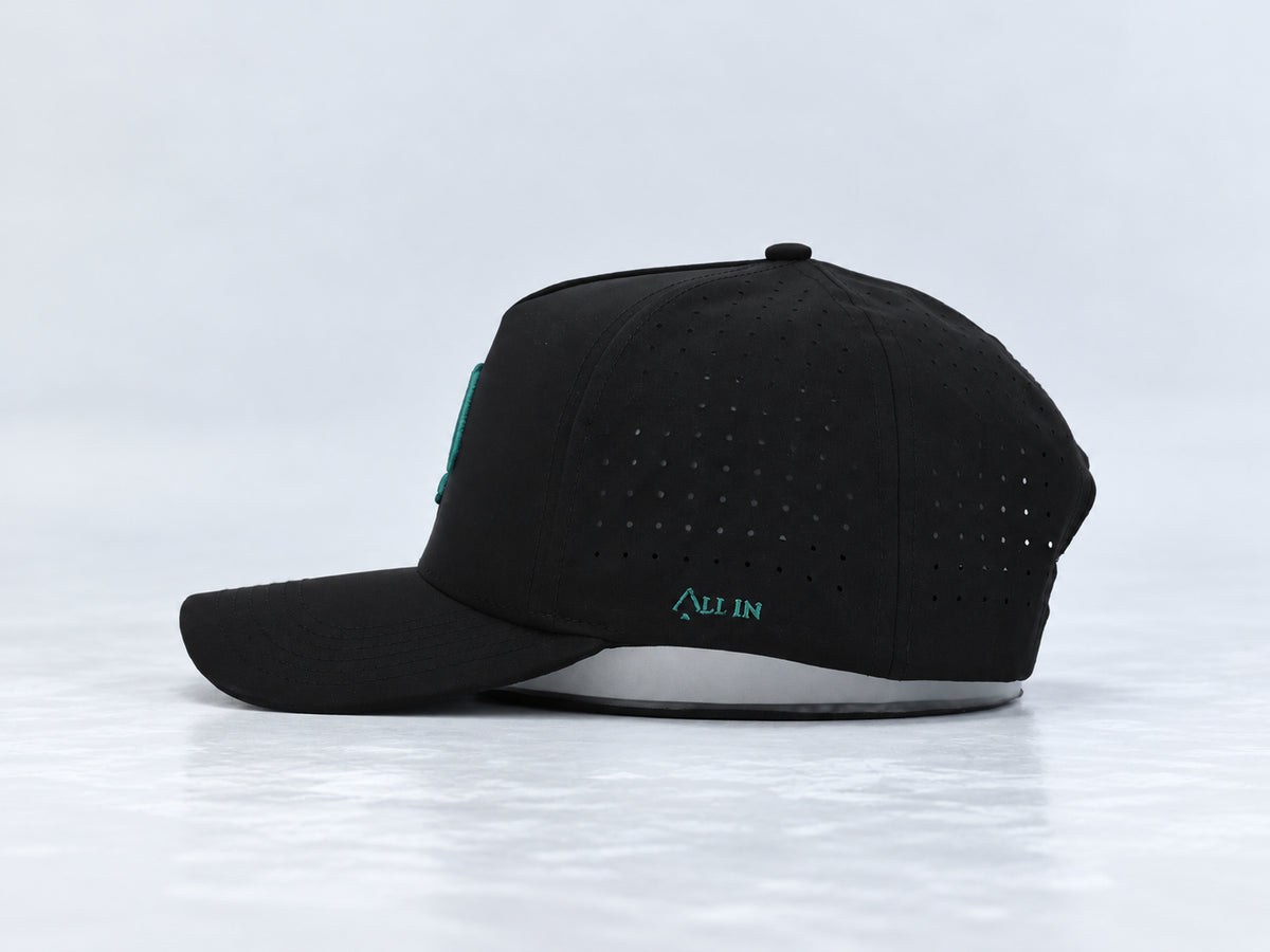 All In Lid Green Goblin black cap, side view with teal green All In embroidery, perforated panels, and a curved brim against a pale gray background.