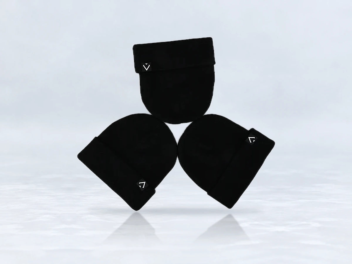 All In Lid Jet Black cuffed beanie in black knit with a white logo patch, flat lay of three beanies, against a pale gray studio background.