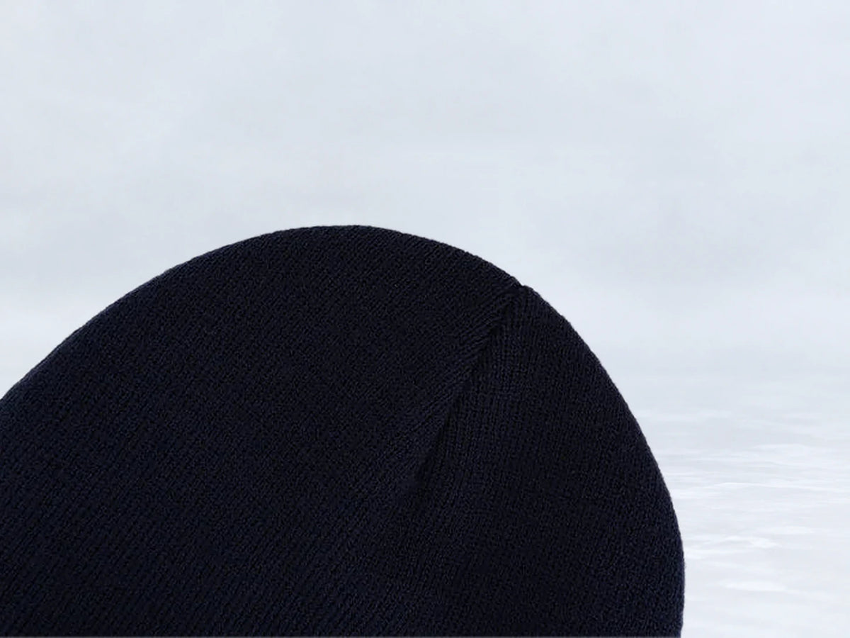 All In Lid Midnight Navy cuffed beanie in navy knit, close-up of the knit crown, against a pale gray studio background.