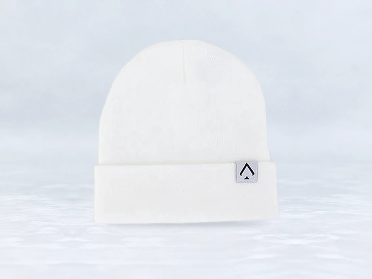 All In Lid Snow White cuffed beanie in white knit with a gray logo patch, front view, against a pale gray studio background.