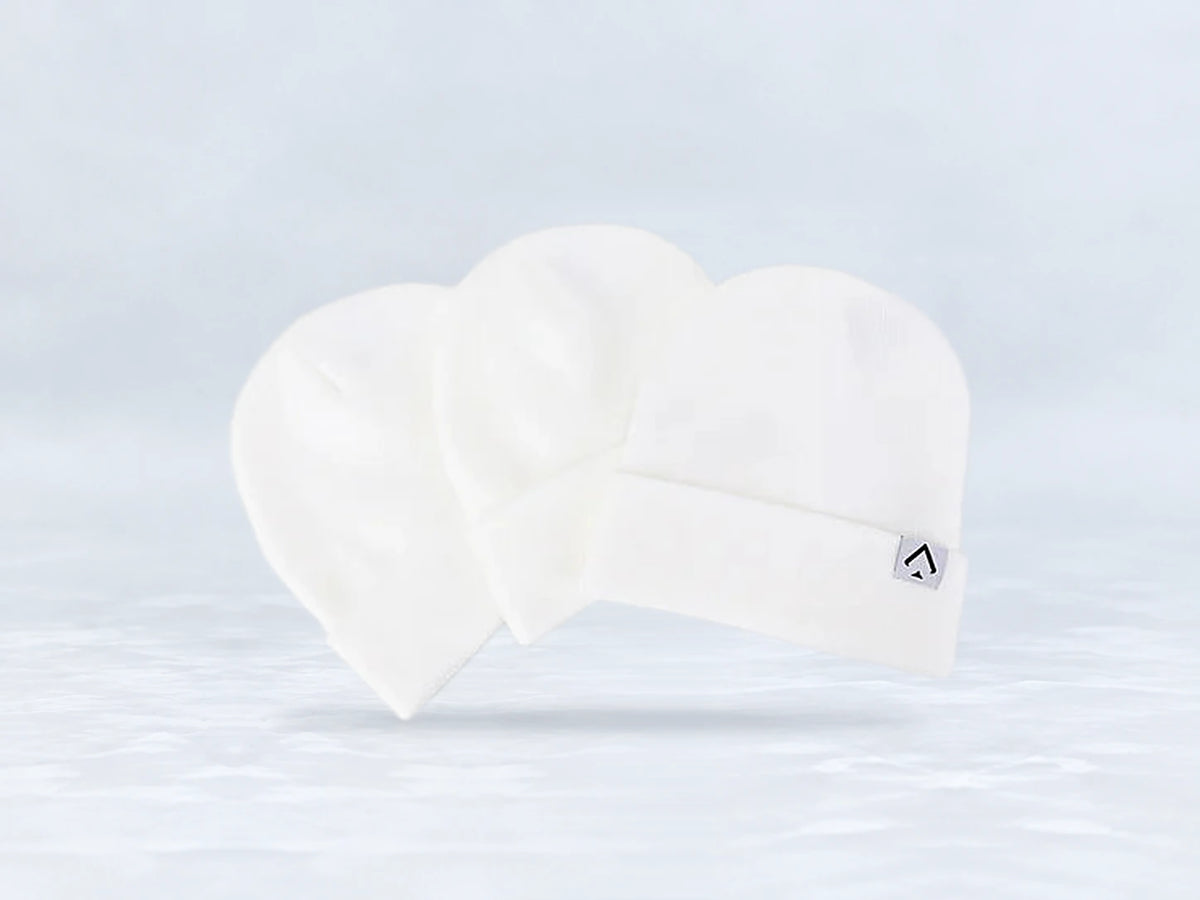 All In Lid Snow White cuffed beanie in white knit with a gray logo patch, three beanies stacked, against a pale gray studio background.