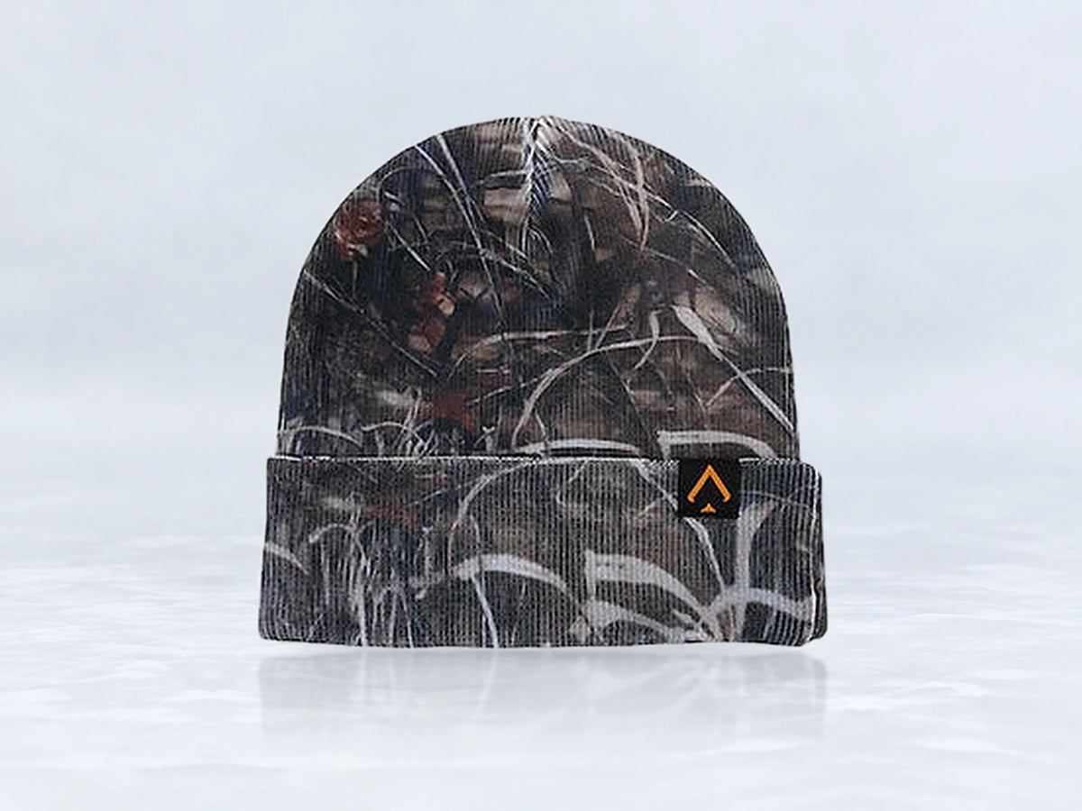 All In Lid Stealth Camo cuffed beanie in woodland camo knit with an orange-outlined logo patch, front view, against a pale gray studio background.