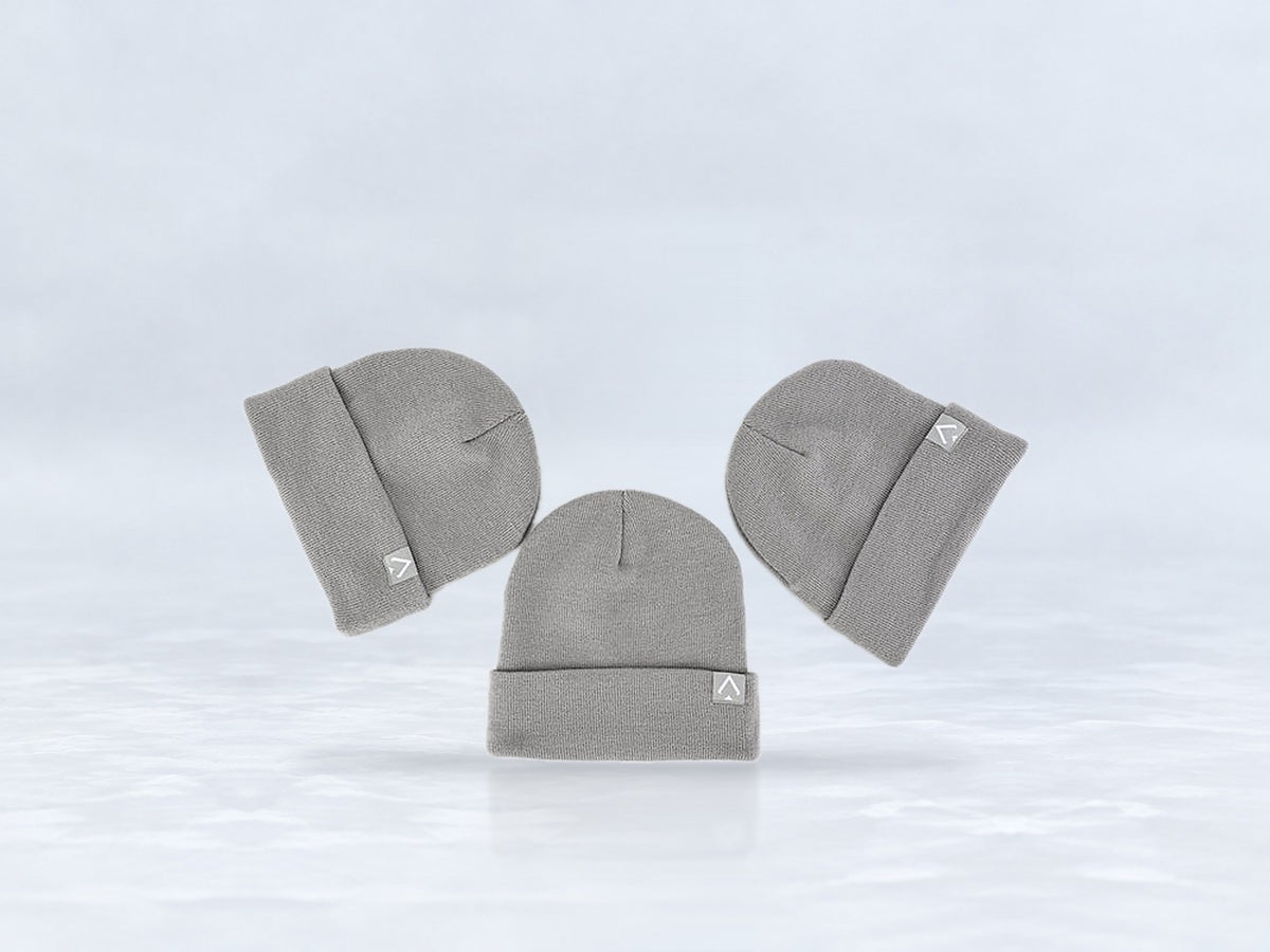All In Lid Ash Gray cuffed beanie in gray knit with a light gray logo patch, flat lay of three beanies, against a pale gray studio background.