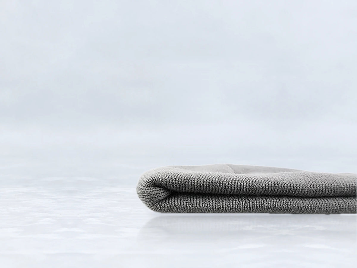 All In Lid Ash Gray cuffed beanie in gray knit, side view of the folded cuff, against a pale gray studio background.
