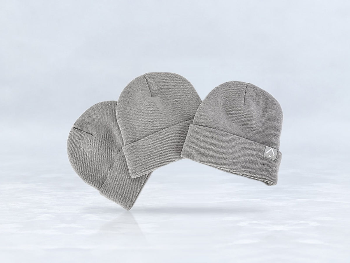 All In Lid Ash Gray cuffed beanie in gray knit with a light gray logo patch, three beanies stacked, against a pale gray studio background.