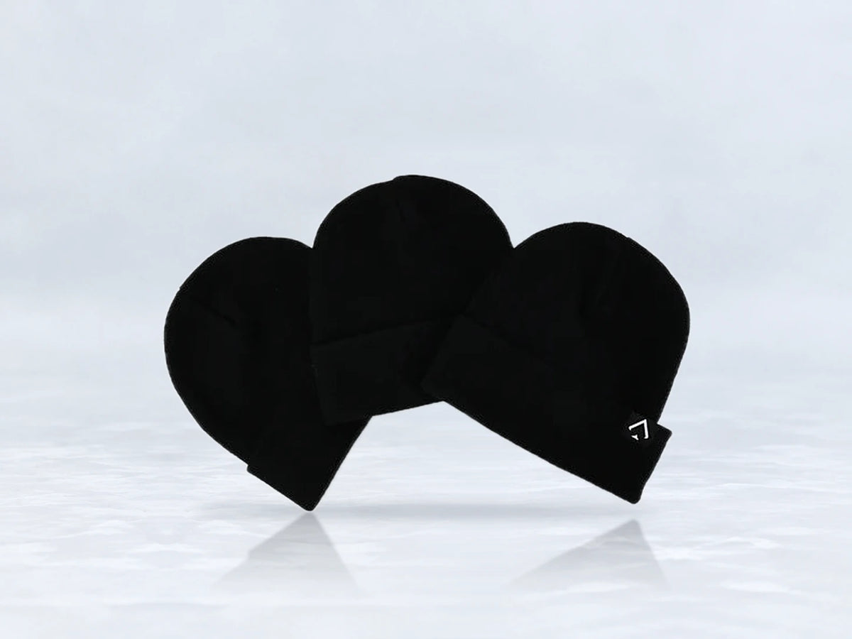 All In Lid Jet Black cuffed beanie in black knit with a white logo patch, three beanies stacked, against a pale gray studio background.