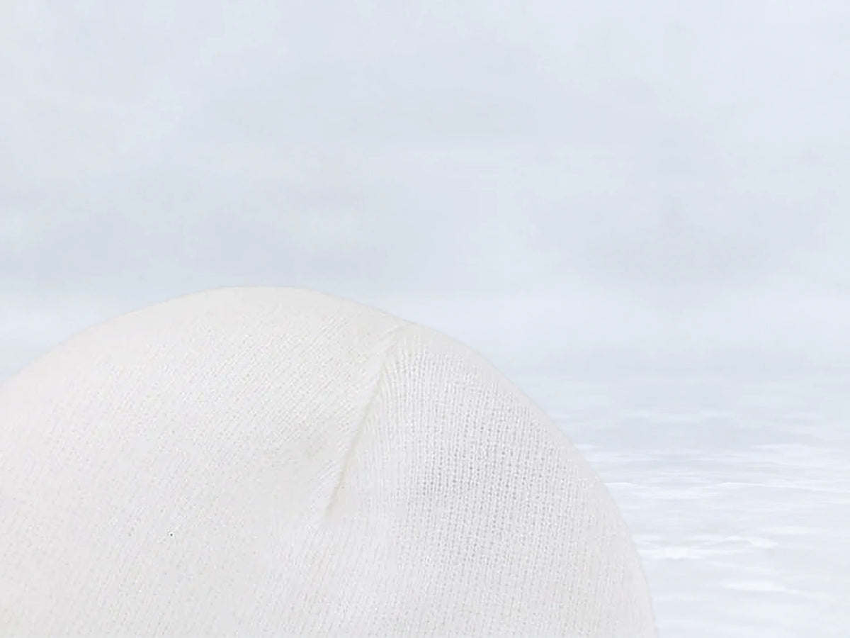 All In Lid Snow White cuffed beanie in white knit, close-up of the knit crown, against a pale gray studio background.