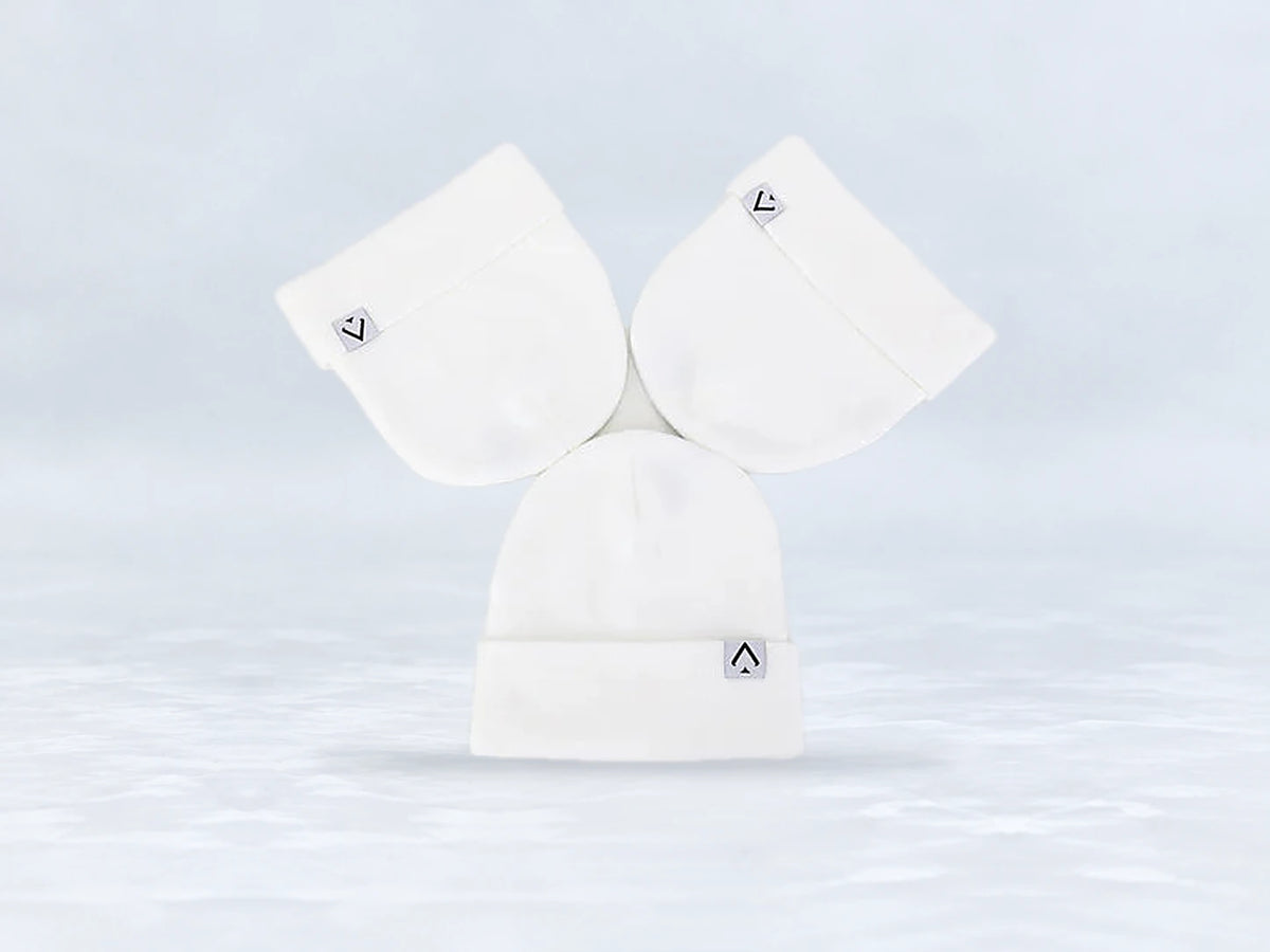 All In Lid Snow White cuffed beanie in white knit with a gray logo patch, flat lay of three beanies, against a pale gray studio background.
