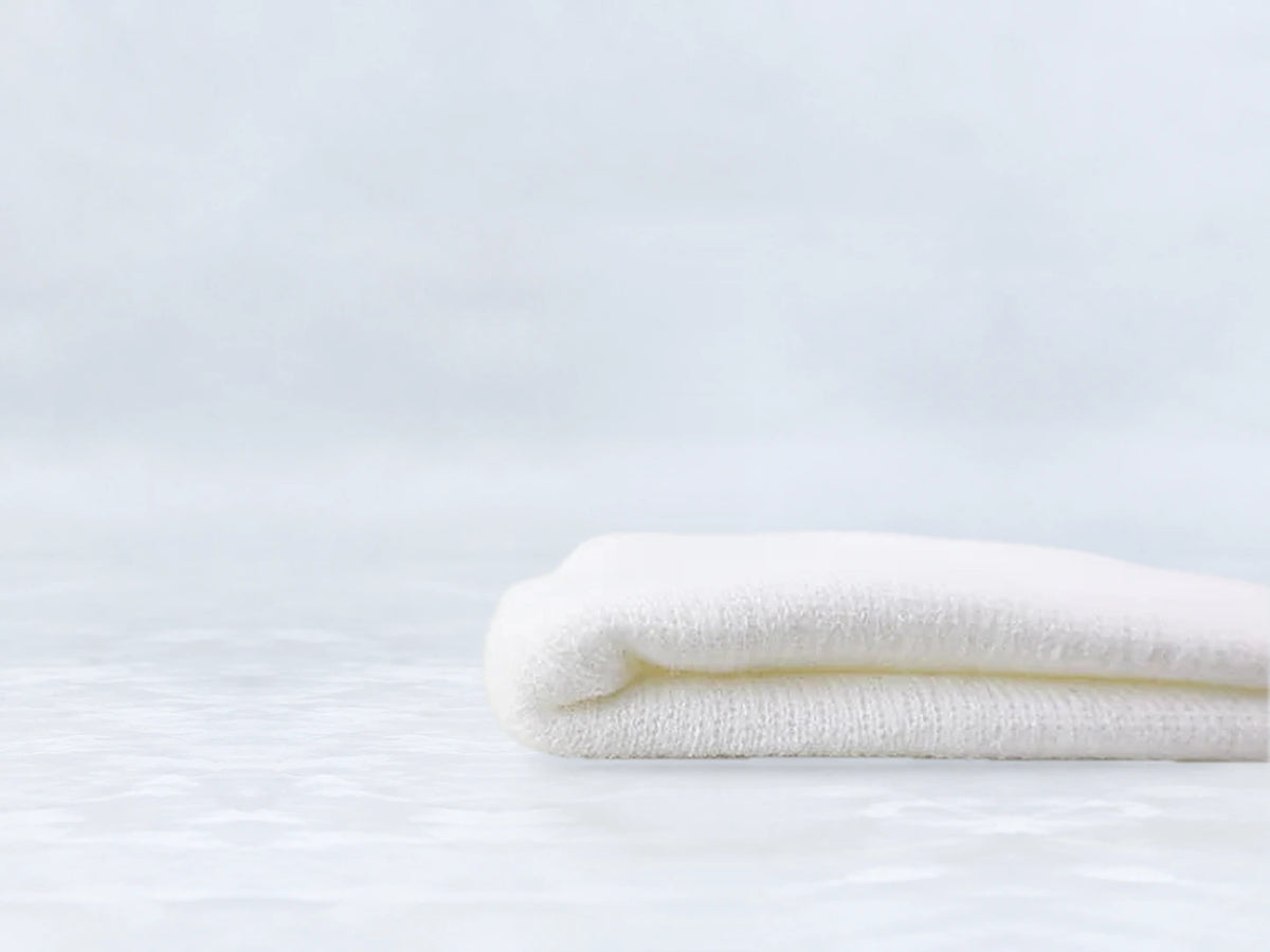 All In Lid Snow White cuffed beanie in white knit, side view of the folded cuff, against a pale gray studio background.