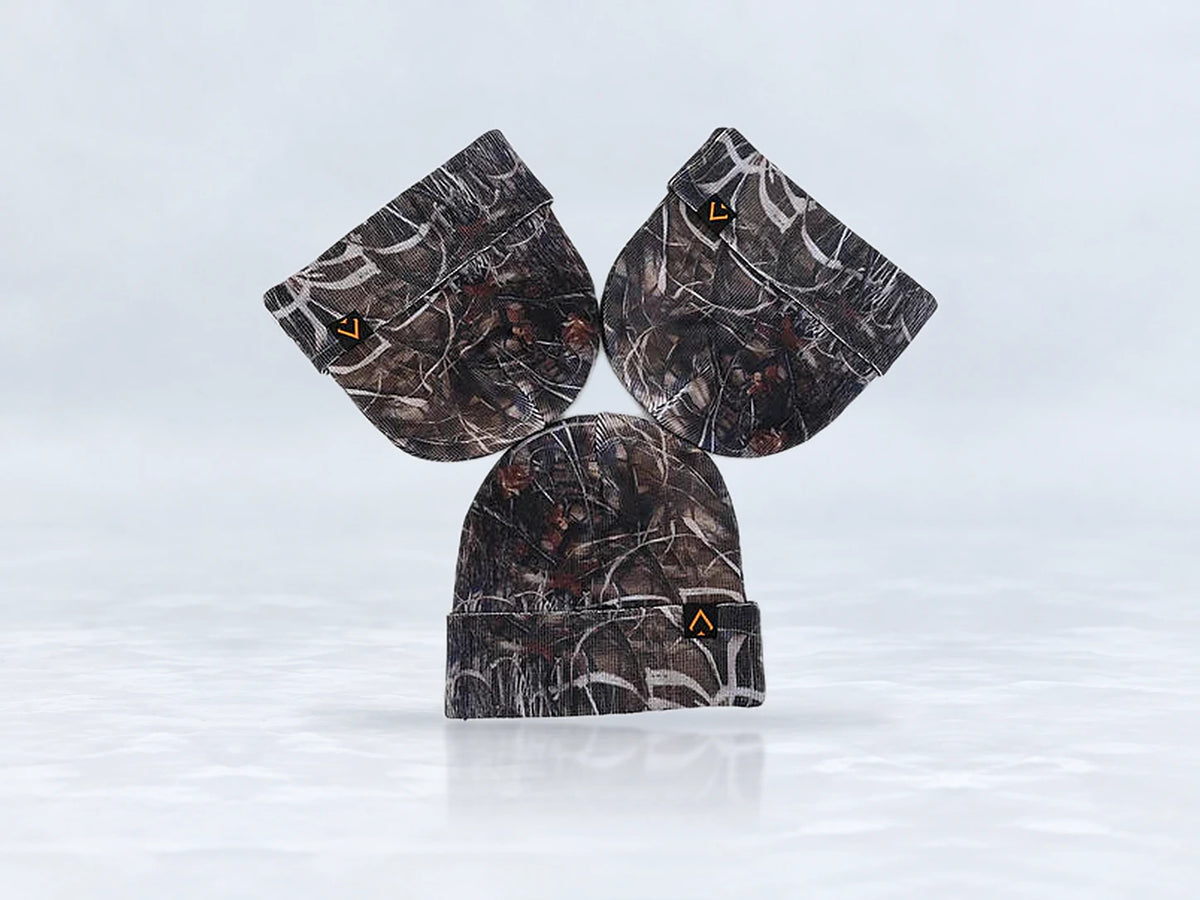 All In Lid Stealth Camo cuffed beanie in woodland camo knit with an orange-outlined logo patch, flat lay of three beanies, against a pale gray studio background.