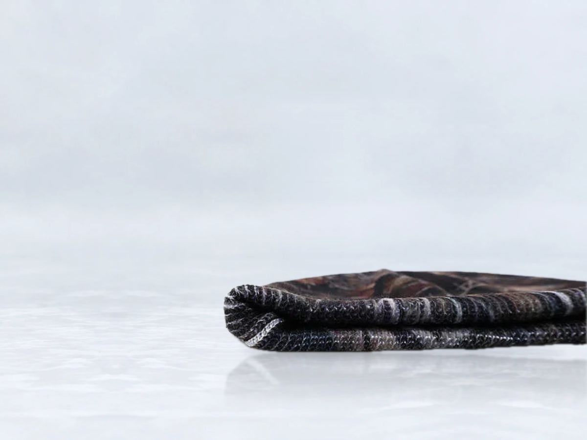 All In Lid Stealth Camo cuffed beanie in woodland camo knit, side view of the folded cuff, against a pale gray studio background.