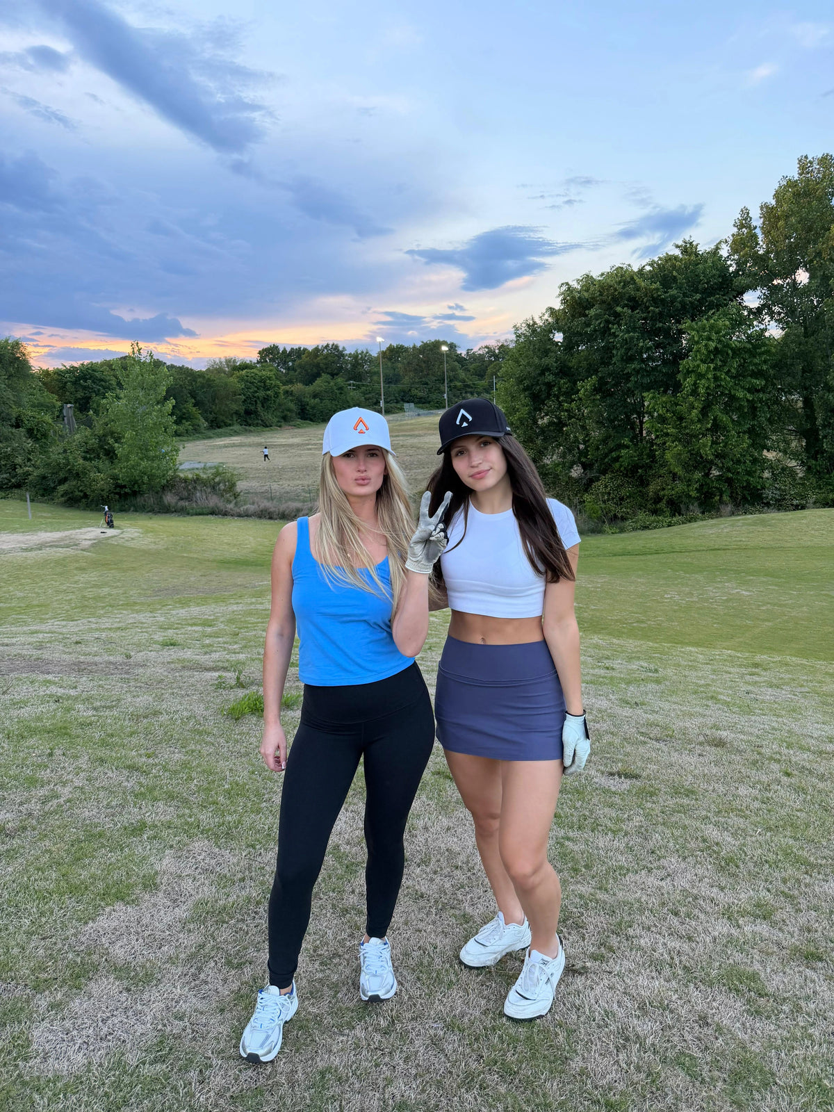 Two women posing on a golf course in white and black All In Lid performance caps.